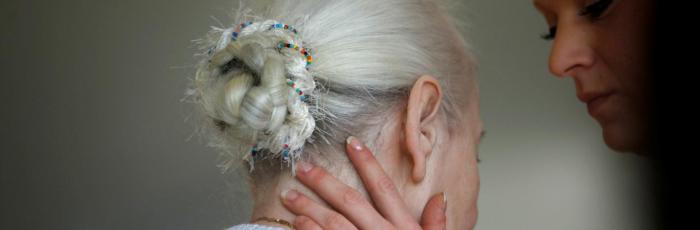 Header Bild: Betreuerin hält eine Frau im Altersheim behutsam am Hals