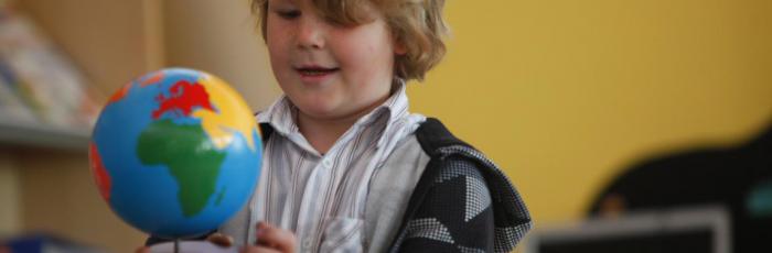 Header Bild: Ein Kind in der Schule untersucht aufgeregt einen Globus
